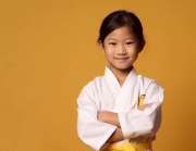 a smiling girl child dressed as a martial arts athletes in soft solid background generative ai